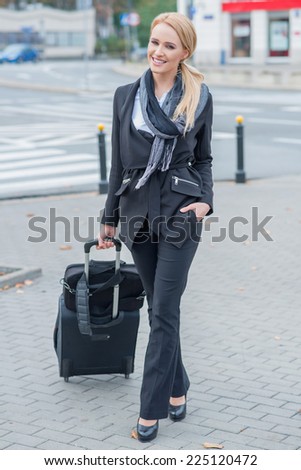 Young businesswoman standing in a stylish outfit in an urban street with a suitcase while on a business trip