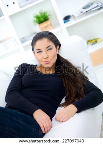 Thoughtful young woman relaxing on a sofa in her living room looking into the air with a contemplative expression  angled view