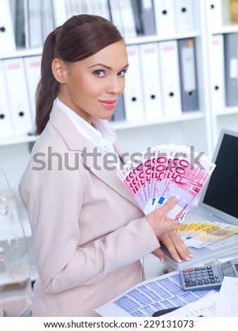Successful elegant female business owner showing off her wealth displaying a fanned handful of 500 euro notes with a smile in her office