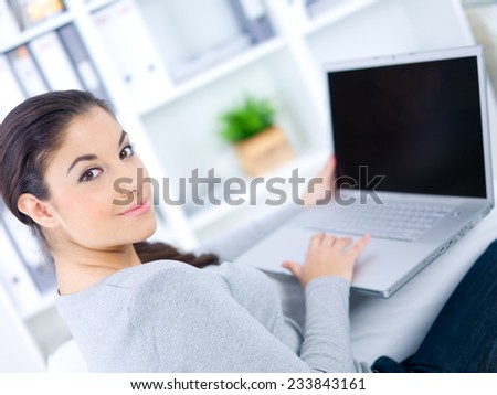 Close up Smiling Pretty Young Woman Sitting on Couch with Laptop Computer While Looking at the Camera.