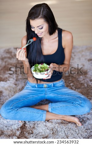 Close up Happy Young Woman Sitting on the Floor with Carpet while Eating Fresh Salad in Bowl.