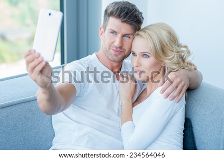 Close up Smiling Young Sweet Lovers in White Shirts Taking Self Photos While Sitting on the Gray Couch.