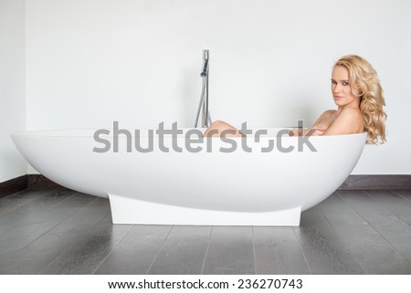Side View of Beautiful Blond Woman Looking at Camera and Relaxing in Modern Bathtub