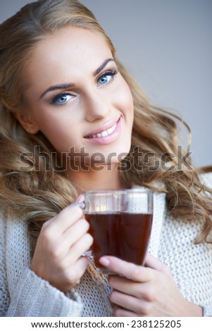 Smiling attractive woman with lovely long curly blond hair enjoying a mug of coffee as she looks at the camera with a friendly smile