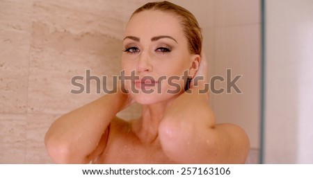 Close up Bare Young Woman Holding the Back of her Head and Looking at the Camera While Taking a Shower at the Bathroom.