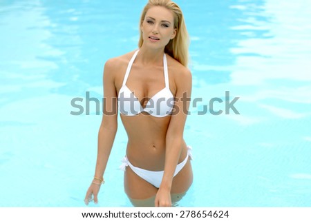 Sexy Young Blond Woman Wearing White Bikini Standing at the Swimming Pool and Looking at the Camera.