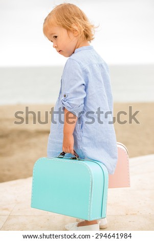 Little girl on vacation at the seaside standing overlooking the beach with her two small suitcases in her hand  side view from behind
