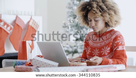 Pretty young African woman buying gifts online for Christmas sitting at her laptop computer entering her credit card details
