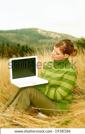 Young business woman holding laptop computer on golden meadow at mountains outdoors