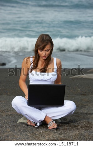 Young beautiful woman on the black beach is using laptop