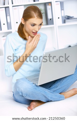 Shocked woman sitting on couch and working on laptop
