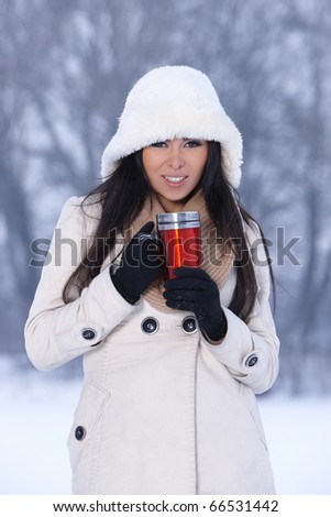 Beautiful woman holding thermal mug in snowy winter outdoors