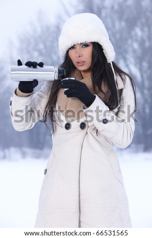 Beautiful woman holding thermos in snowy winter outdoors