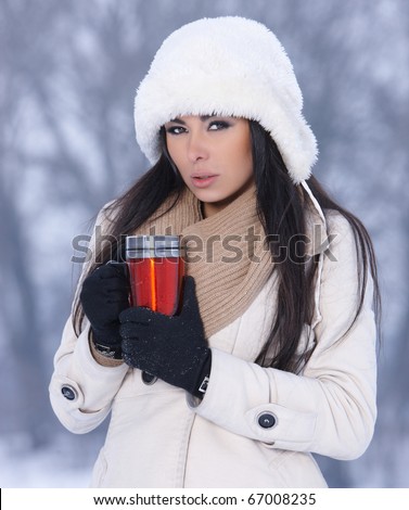 Beautiful woman holding thermal mug in snowy winter outdoors