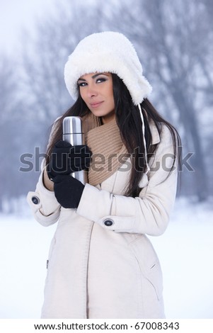 Beautiful woman holding thermos in snowy winter outdoors