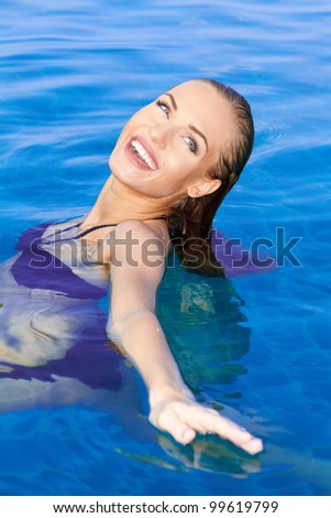 Beautiful woman with a lovely smile relaxing in a sparkling pool with her head tilted back.