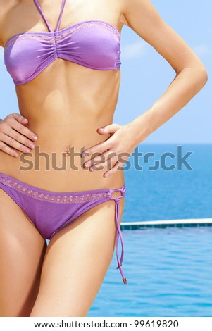 Cropped image of a female hand resting lightly on the curvy buttocks of a woman in a bikini against blue sky.