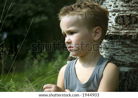 Six year old sitting against a tree being sad and thinking