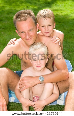 Happy family picture of a father and two sons sitting at the grass in summertime.