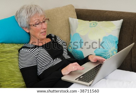 Senior woman working on a laptop, lying relaxed on the couch.