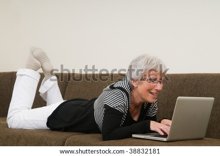 Senior woman working on a laptop, lying relaxed on the couch.