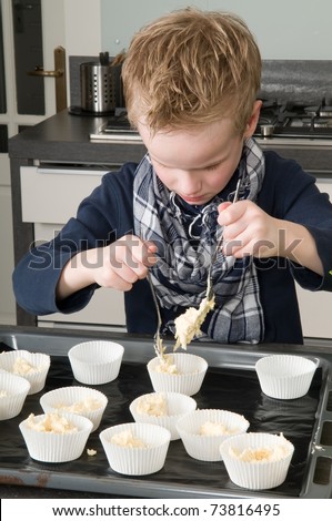 Kid filling the cakecups with the dough, for baking cakes.
