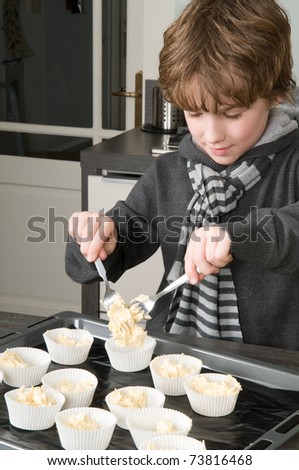Kid filling the cakecups with the dough, for baking cakes.
