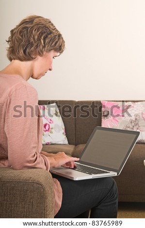 Young woman working at home on a laptop, from behind