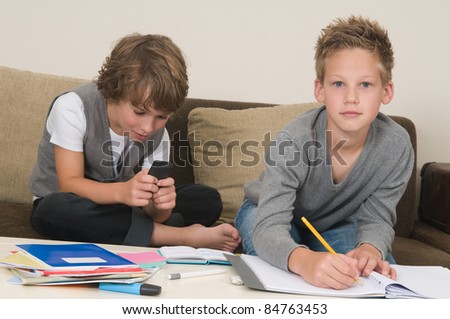 Two friends doing their homework in the livingroom. One of them is gaming, the other one is not ready and is jealous.