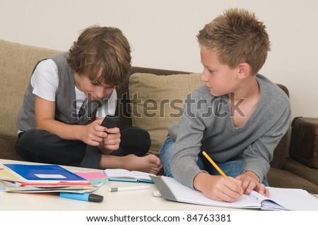 Two friends doing their homework in the livingroom. One of them is gaming, the other one is not ready and is jealous.