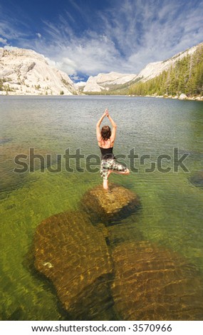A fit woman stands in a yoga pose named The Tree on a rock in a lake in Yosemite national park.