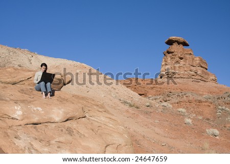 A beautiful woman displays the miracle of wireless connectivity and laptop computers as she surfs the web in the middle of the desert.