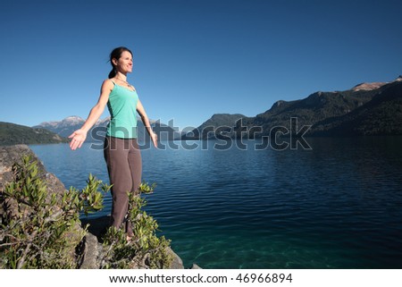 A woman begins a sun salutation near a clear blue lake in Argentina.
