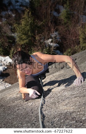 A strong woman struggles up a steep rock face in Squamish British Columbia Canada.