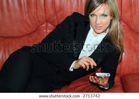 A young businesswoman makes notes on her PDA (pocket pc) sitting on the couch