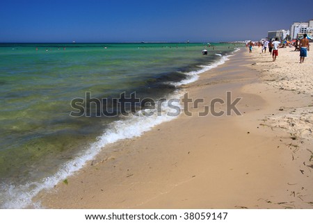Very bright day, beautiful clear water, clear wave breaking into shore. Bright blue sky, minimal cloud cover. Tunis.