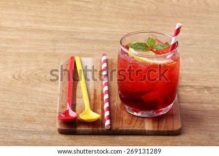 cold red soft drink from raspberry syrup and mint with red straw on wooden board