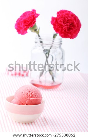 red homemade strawberry ice cream and red carnation flower in glass mason jar on white background