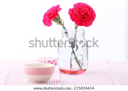 pink ceramic cup and red carnation flower in glass mason jar on white background
