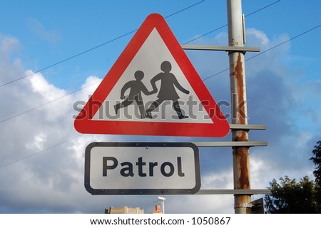 School crossing patrol sign attached to a rusty pole with a blue sky background.