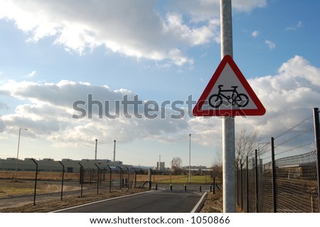 A red triangle end of cycle way sign on a post with the end of the cycleway in sight.