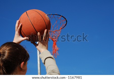 Young girl about to try and score at basketball against a blue sky background.