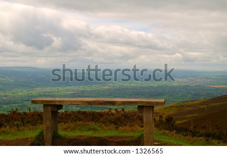 Wooden bench on a mountain walk with a great view over the countryside below,with rolling clouds and patches of blue sky.