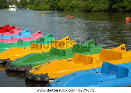Pedal boats of various colours all lined up at the river bank waiting to be used with river scene in the background.
