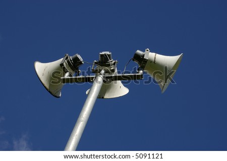 Public address system comprising of three tannoy speakers on a pole with a blue sky background