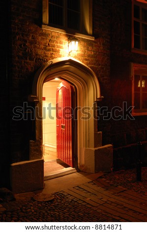 Old fashioned wooden door open and inviting from a dark cobbled street