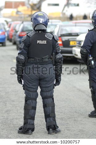 Uk police officer in full riot gear at the scene of a public disturbance.
