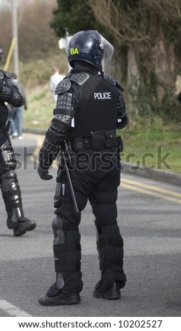 Uk police officers in full riot gear at the scene of a public disturbance.