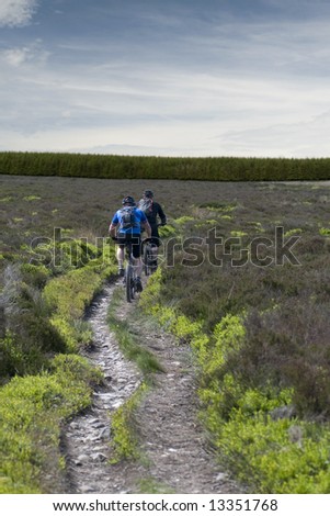 Two mountain bikers cycling on a dirt trail in the countryside