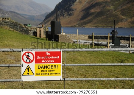 Warning sign on a gate saying no unauthorised access and advising of deep water and strong currents with Ennerdale lake in the English Lake District in the background